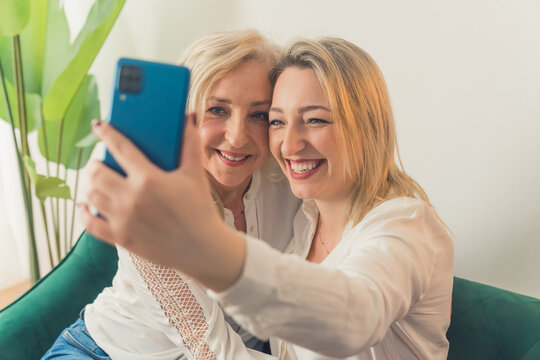 Joyful beautiful attractive middle-aged women sitting on a green couch making a selfie with a smartphone with a blue case. High quality photo