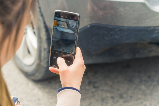 Outdoor shot of an unrecongnizable caucasian woman taking a photo on a road of her cars front fender with a modern smartphone. High quality photo