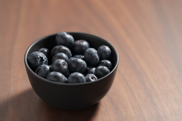 Blueberries in black ceramic bowl on walnut table