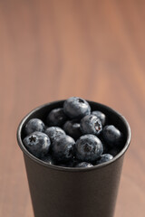 Blueberries in black paper cup on walnut table