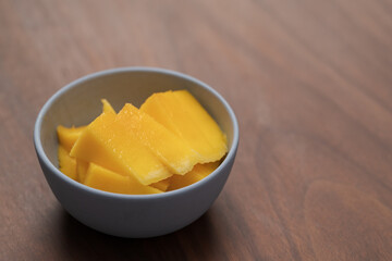 Fresh sliced mango in a ceramic bowl on walnut table