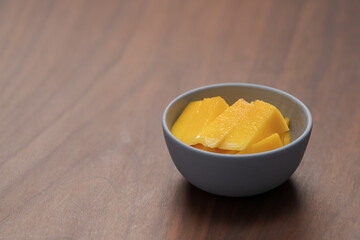 Fresh sliced mango in a ceramic bowl on walnut table