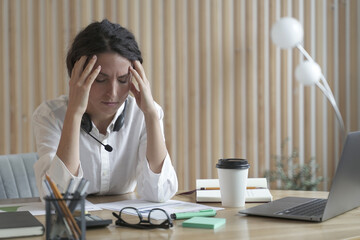 Tired spanish businesswoman with closed eyes sitting at workplace in office, suffering from headache