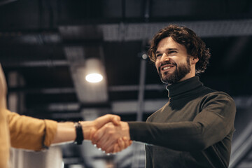 Business partnership. Smiling entrepreneur handshaking with partner after successful negotiations at modern office