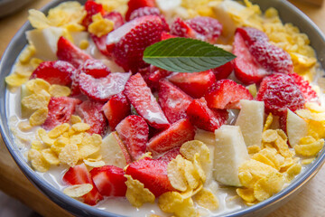 Cornflakes with oat milk and fruit - apple, pear and strawberries decorated with mint leaf