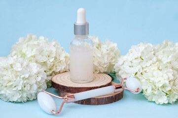 Serum for face care and a massage roller for the face on a wooden podium against a background of white flowers