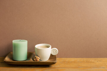 Cup of coffee and candle on wooden table. brown wall background