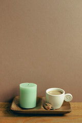 Cup of coffee and candle on wooden table. brown wall background