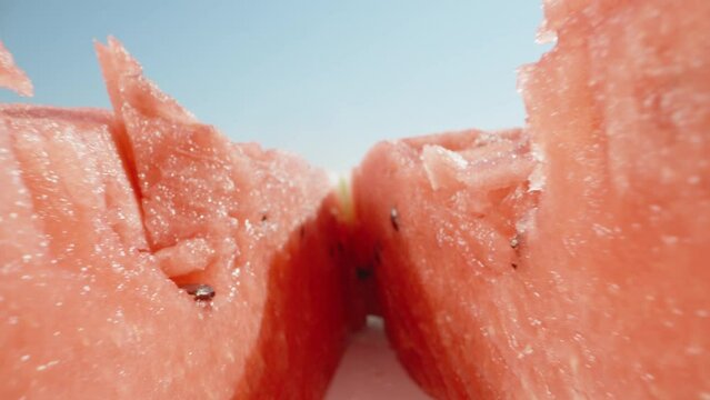 The watermelon is torn in half and the camera rolls inside. Against the blue sky. Dolly slider extreme close-up. Laowa Probe. Slow mo