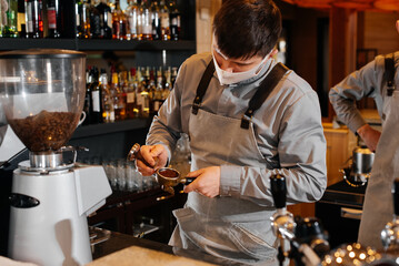 A masked barista prepares an exquisite delicious coffee at the bar in a coffee shop. The work of restaurants and cafes during the pandemic.