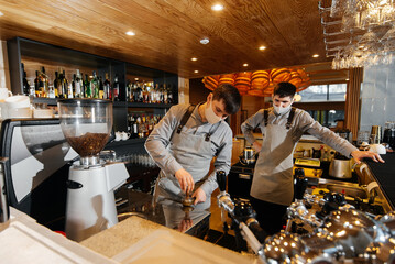 Two masked baristas prepare exquisite delicious coffee at the bar in the coffee shop. The work of...