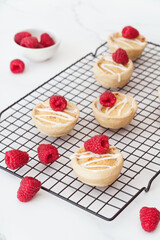 Home baked raspberry bakewell tarts decorated with icing and fresh raspberries. Light and airy style food image with white background and copy space