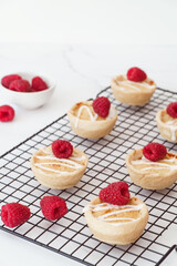 Home baked raspberry bakewell tarts decorated with icing and fresh raspberries. Light and airy style food image with white background and copy space