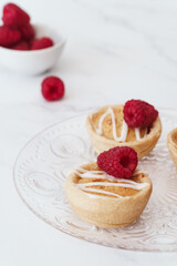 Home baked raspberry bakewell tarts decorated with icing and fresh raspberries. Light and airy style food image with white background and copy space