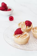 Home baked raspberry bakewell tarts decorated with icing and fresh raspberries. Light and airy style food image with white background and copy space