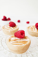 Home baked raspberry bakewell tarts decorated with icing and fresh raspberries. Light and airy style food image with white background and copy space