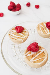 Home baked raspberry bakewell tarts decorated with icing and fresh raspberries. Light and airy style food image with white background and copy space