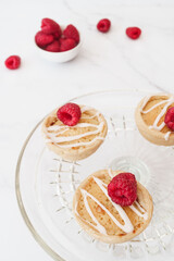 Home baked raspberry bakewell tarts decorated with icing and fresh raspberries. Light and airy style food image with white background and copy space