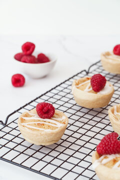 Home baked raspberry bakewell tarts decorated with icing and fresh raspberries. Light and airy style food image with white background and copy space