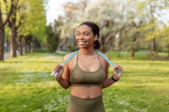 Joyful young black woman in sports clothes posing with jumping rope at park. Active lifestyle concept