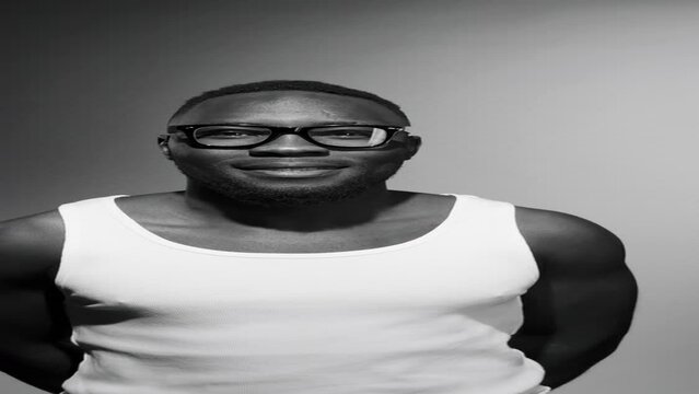 Vertical black and white shot of young handsome African American man in tank top and glasses smiling and posing for camera in studio