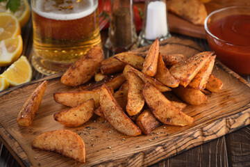 Rustic spicy fried potato slice on a wooden plate, with tomato sauce and beer