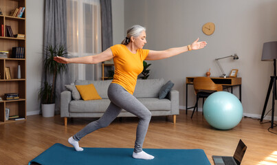 Online yoga training. Active senior woman exercising in front of laptop, having online yoga class...