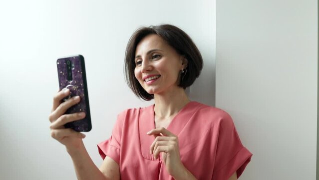 Smiling millennial female holding smartphone talking by video call wave hand to camera. Positive young mixed race woman contact call friend by video link chat using device webcam