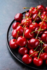 Obraz na płótnie Canvas Red cherry on a black plate. Sweet cherries on a dark background. Freshly picked delicious red berries