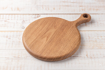 round cutting board with a handle on a white wooden table. mockup of a food background with copy...