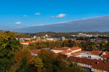 Aerial panorama view of Graz cityscape from Schlossberg in northeast of LKH hospital and Mariatrost direction on a sunny day in autumn, with blue sky cloud and colorful trees, Graz, Styria, Austria