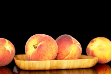 Several sweet organic peaches on a wooden tray, close-up, isolated on a black background.