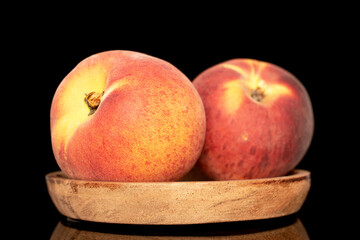 Two sweet organic peaches on a wooden saucer, close-up isolated on a black background.