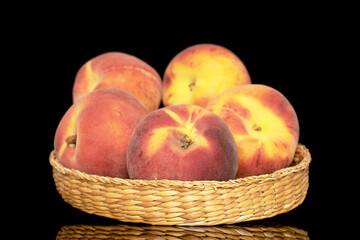 Several sweet organic peaches on a straw plate, close-up, isolated on a black background.
