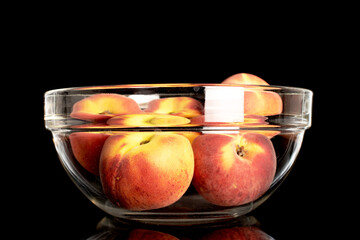 Several sweet organic peaches in a glass bowl, close-up, isolated on a black background.