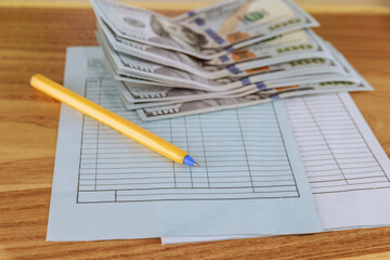 Hundred dollar bills pen and accounting notebooks lie on a wooden table.