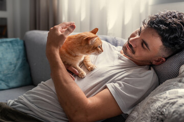 Obraz na płótnie Canvas close up. young man lying on a sofa, hugs a brown tabby cat