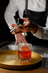 hand of bartender pours bright alcoholic drink from jigger into crystal glass