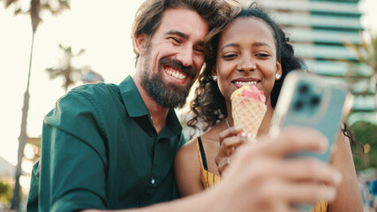 portrait of happy man and smiling woman watching video on smartphone. Close-up of joyful young interracial couple browsing photos on mobile phone on urban city background