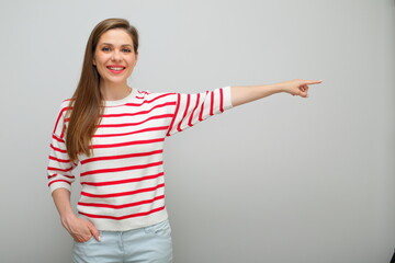 Smiling woman finger pointing  to copy space on background, isolated female studio portrait, girl in white sweater with red stripes..