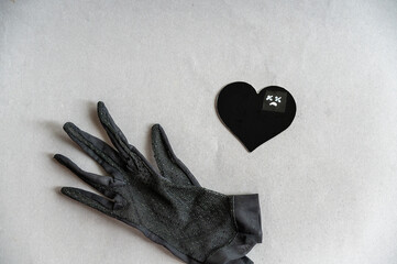A black lace glove and a paper heart against a gray background. A sad face with crosses over the...