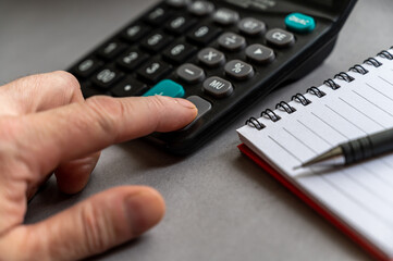 Close-up of a man's hand doing calculations on a calculator. The index finger presses the EQUAL...