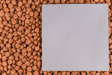 A gray and lilac piece of paper lies on top of the dog food. Brown pellets of dry pet food. Empty...