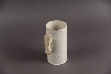 An empty sleeve of toilet paper against a gray background. Cylindrical sleeve with a small piece of toilet paper. Selective focus.