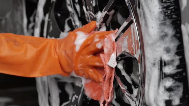 Close up of car wash worker wearing protective gloves and washing car with soapy sponge. Cleaning services.