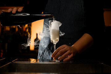 glass with steaming cocktail into which bartender accurate pours drink from bottle