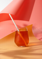 Cold refreshing drink in the heat. Kombucha in a glass with a tube. Bright background, pink, yellow, vertical format
