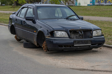 Fototapeta premium Old abandoned rusty car without license plates and wheels on the side of the road