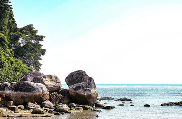 Big boulders that are on the edge of a beautiful beach with a blue sky