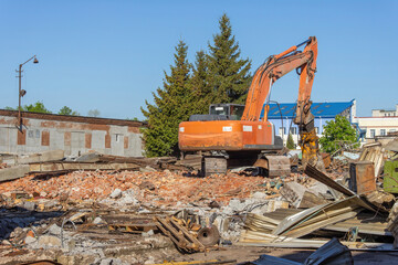 Demolition of obsolete dilapidated buildings. A large orange excavator stands on the rubble of a demolished building.